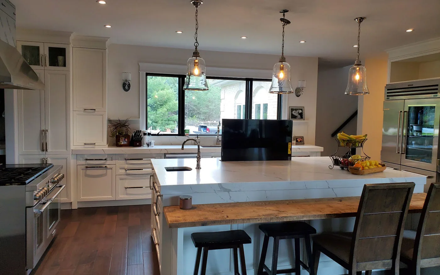 Open kitchen with a marble island, live edge walnut bar top and a television lift