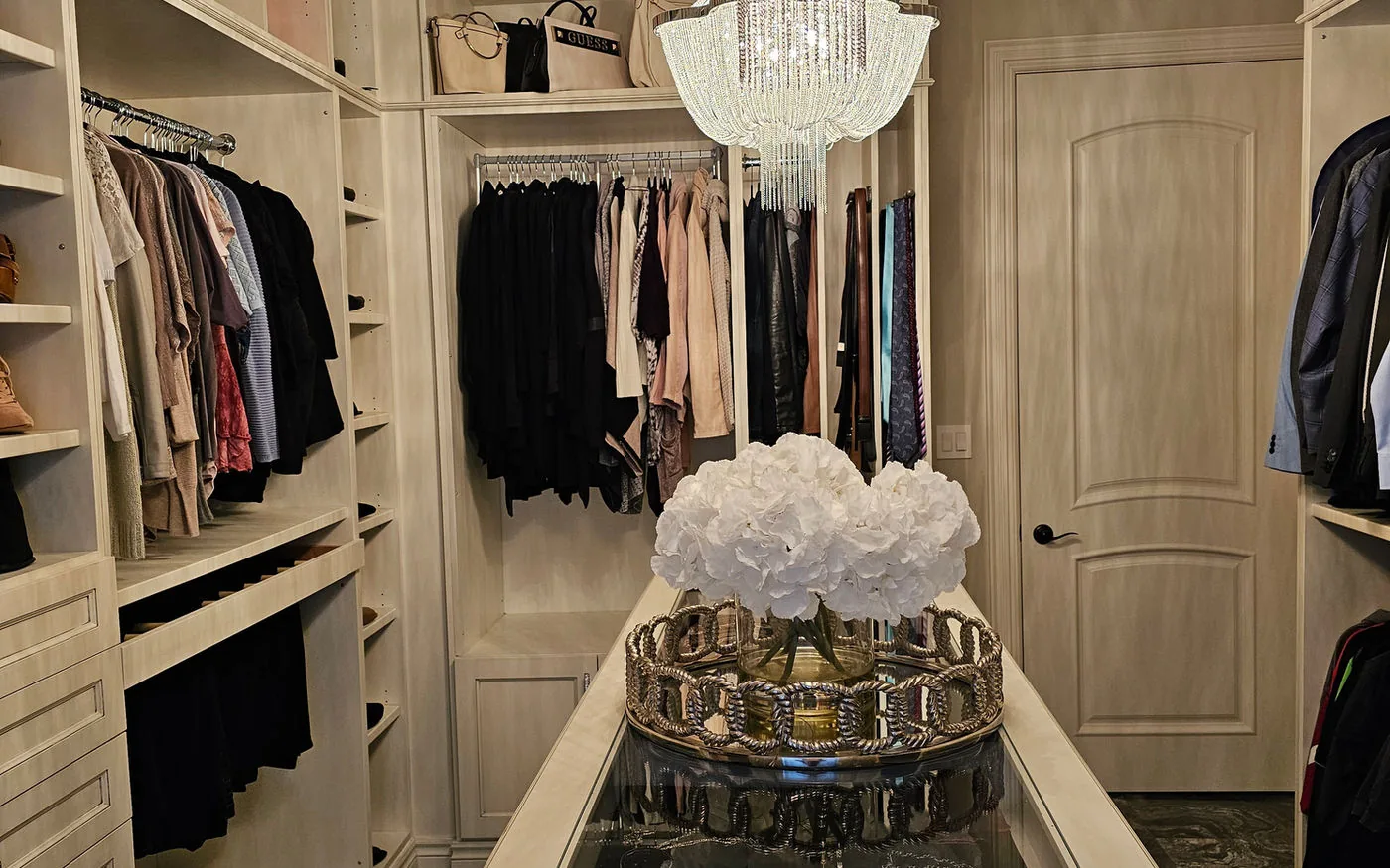 Walk in closet with built in cabinetry, a glass topped island and a crystal chandelier