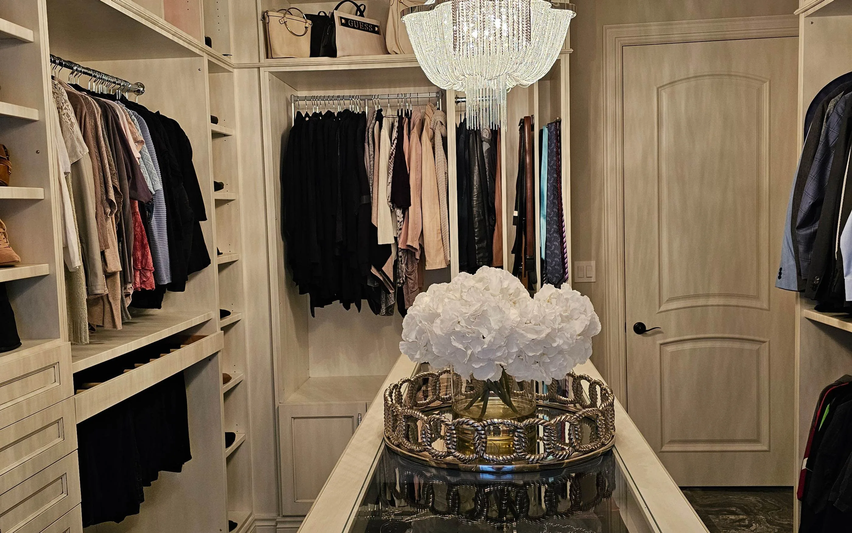 Walk in closet with built in cabinetry, a glass topped island and a crystal chandelier