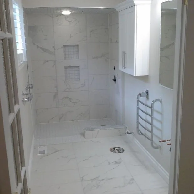 Curbless marble tiled shower with a bench, niche and a linear drain