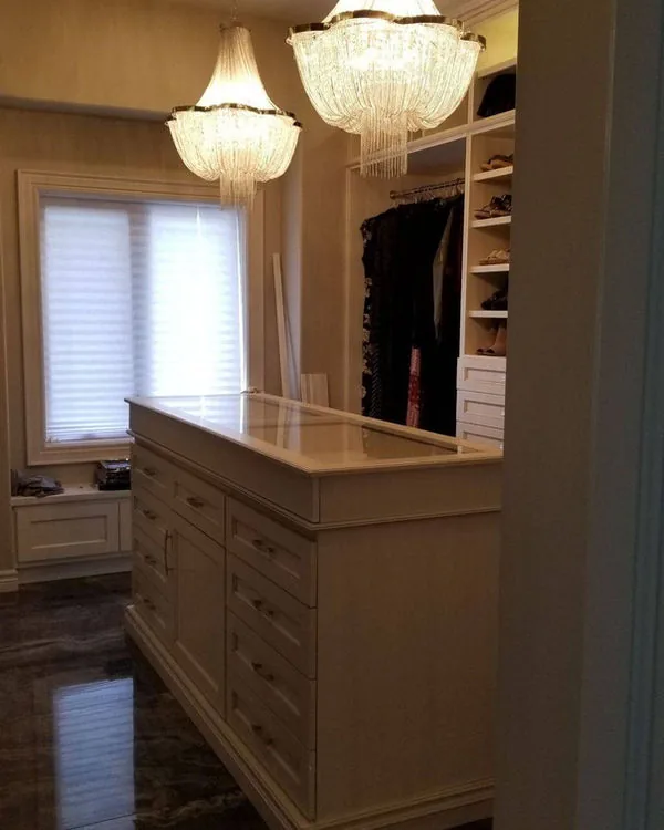 Walk in closet with a drawer island, chandeliers and full height hanging cabinetry