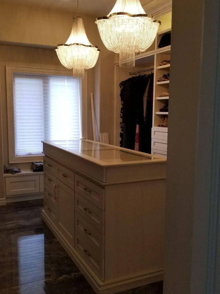 Walk in closet with a drawer island, chandeliers and full height hanging cabinetry