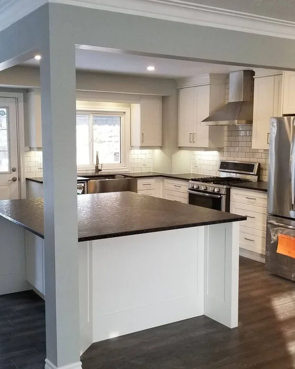 White kitchen with dark stone counters, a peninsula and a stainless hood