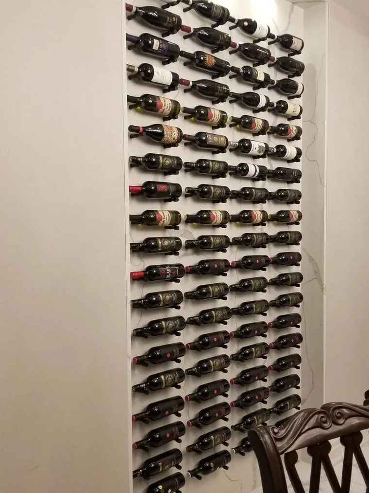 Floor to ceiling wine wall with metal peg racking holding several dozen bottles